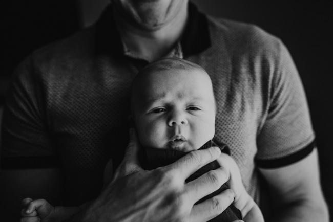 black and white image of newborn face held by fathers hand with lifestyle newborn photographer Perth