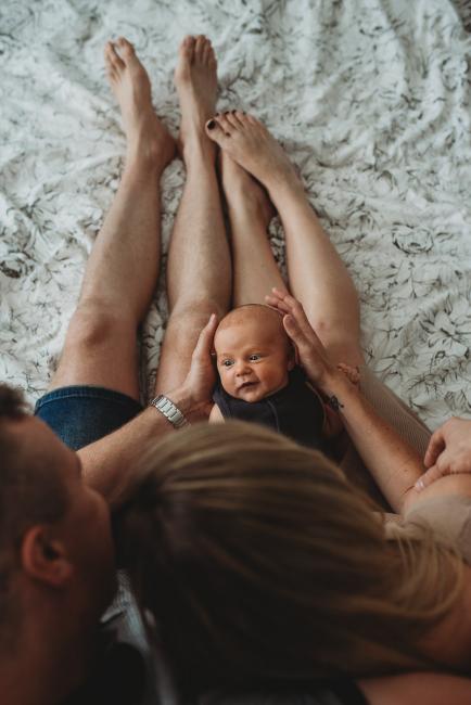 Newborn baby smiling as he lays across parents laps with Perth newborn lifestyle photographer