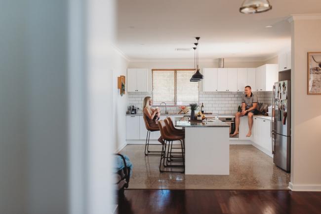 Father sitting on kitchen bench as mother feeds newborn baby on bar stool with Perth lifestyle newborn photographer