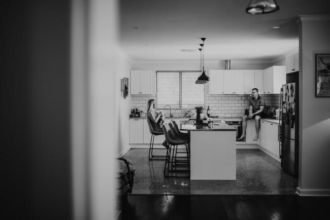 Lifestyle-Newborn-Photographer-Perth-47-of-69 black and white image of father sitting on kitchen bench while mother feeds newborn baby on bar stool with Perth lifestyle newborn photographer