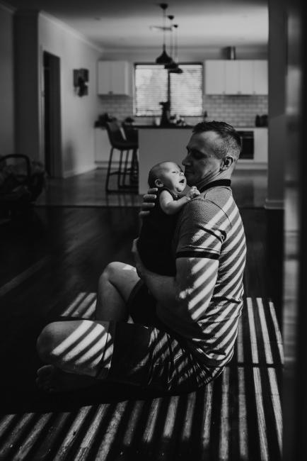 Lifestyle-Newborn-Photographer-Perth-50-of-69 Black and white image of father sitting in hard light with newborn baby with Perth lifestyle newborn photographer