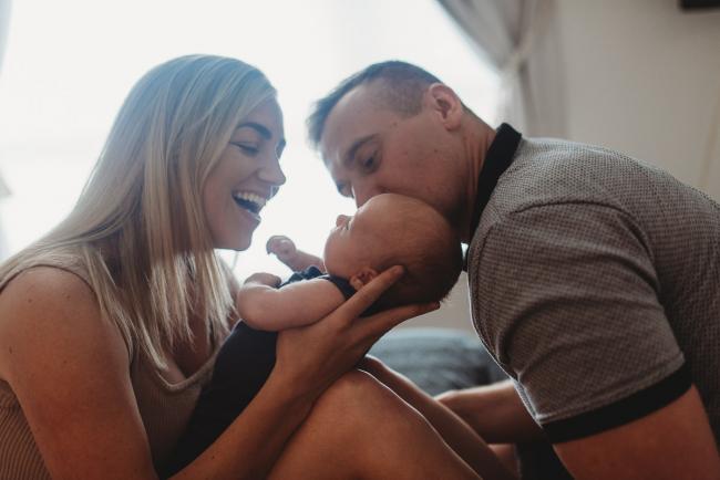 Father kissing newborn baby as mother smiles with Perth lifestyle newborn photographer