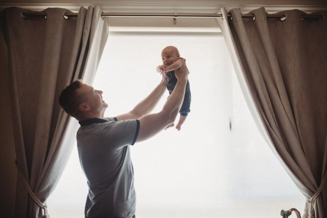 Lifestyle-Newborn-Photographer-Perth-67-of-69 Father lifting newborn baby into the air in front of window with Perth lifestyle newborn photographer