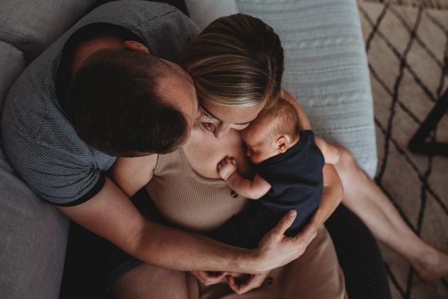 Mother holding newborn baby on couch as father cuddles them with lifestyle newborn photographer Perth