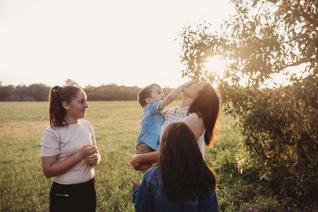 Little boy touching mothers face as sisters look on during Perth family photographer session at Perry's Paddock