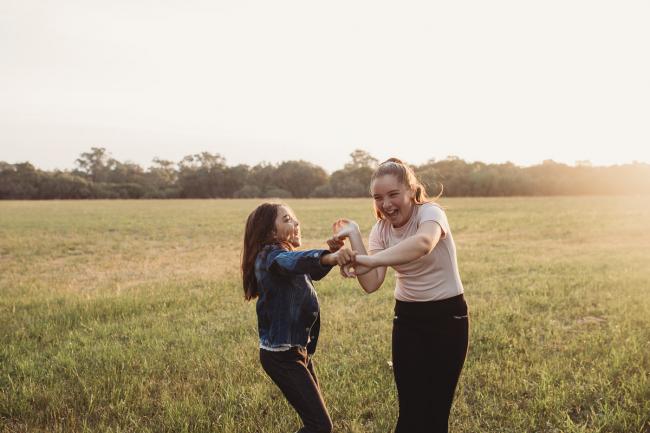 Sisters holding hands and laughing during Perth family photographer session at Perry's Paddock