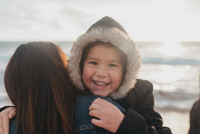 Family-Photographer-Perth-Burns-Beach-1-of-57 Girl in hoodie looking over her mum's shoulder at Burns Beach with Perth Family Photographer