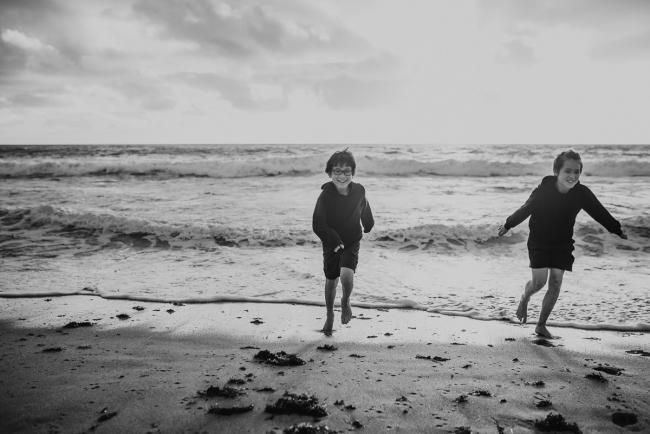 Black and white image of brothers running out of the water at Burns Beach with Perth Family Photographer
