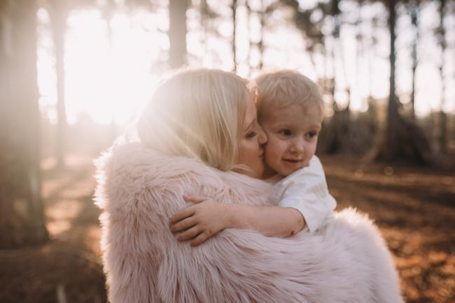 Family-Photographer-Perth-The-Pines-20-of-29 mother kissing son with sun flare during Perth family photography session at The Pines Wanneroo