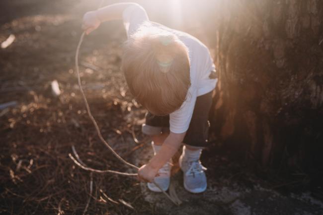 Family-Photographer-Perth-The-Pines-24-of-29 boy bending down and playing with stick during Perth family photography session at The Pines Wanneroo