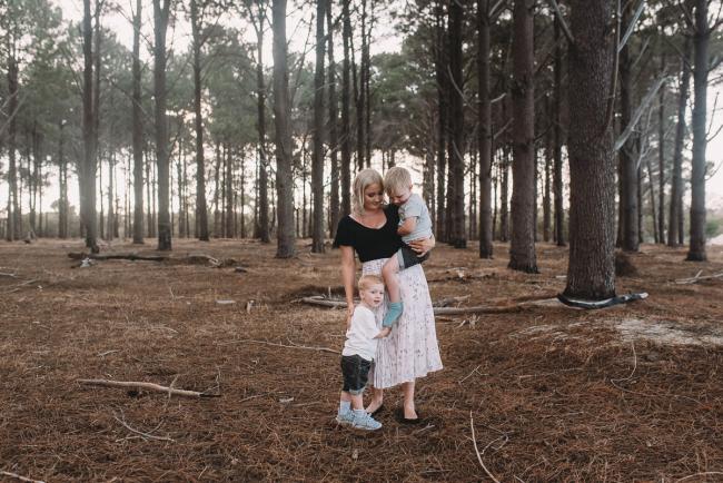 Family-Photographer-Perth-The-Pines-7-of-29 Mother holding one son while the other son hugs her legs during Perth family photography session at The Pines Wanneroo