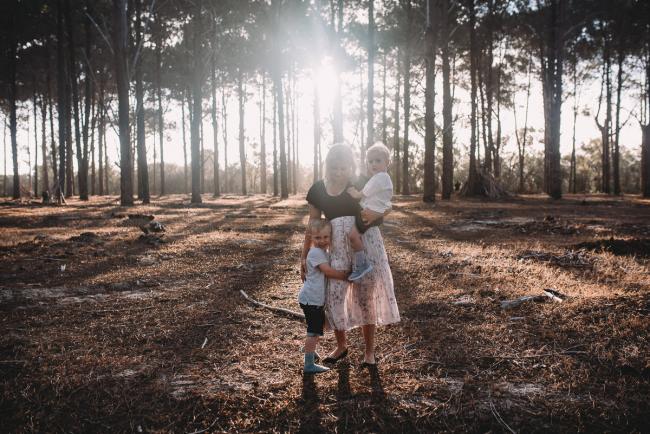 Family-Photographer-Perth-The-Pines-9-of-29 Mother holding one son while the other son hugs her legs during Perth family photography session at The Pines Wanneroo