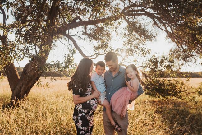 Father holding son and daughter next to pregnant mother during Perth maternity photography session during golden hour at Perry's Paddock