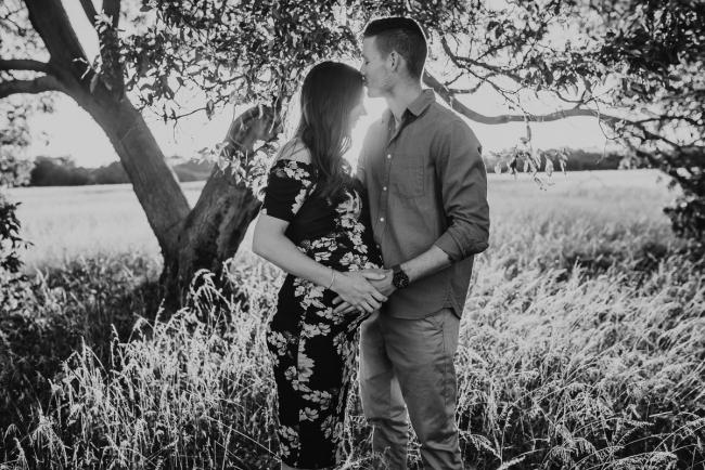 black and white image of husband kissing pregnant wife's forehead during Perth maternity photography session during golden hour at Perry's Paddock