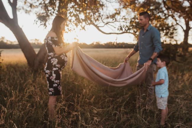 Parents laying out blanket on grass with boy next to them during Perth maternity photography session during golden hour at Perry's Paddock