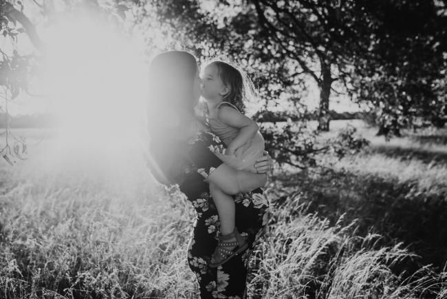 black and white image of little girl sitting on pregnant mums tummy while kissing her during Perth maternity photography session during golden hour at Perry's Paddock