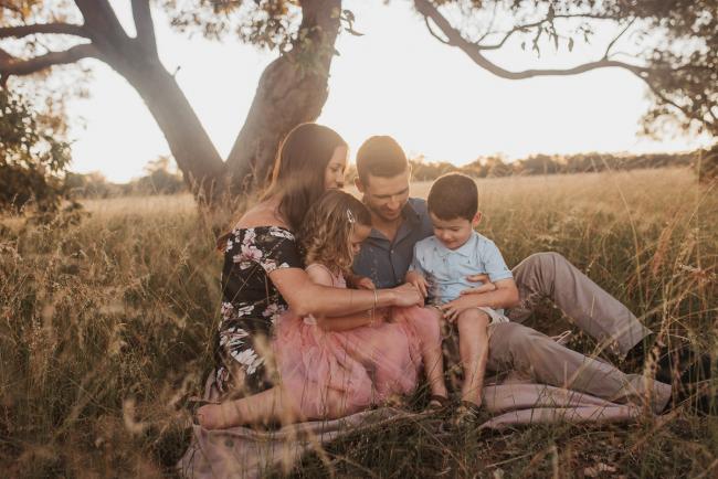 Family of four sitting on blanket under trees during Perth maternity photography session during golden hour at Perry's Paddock