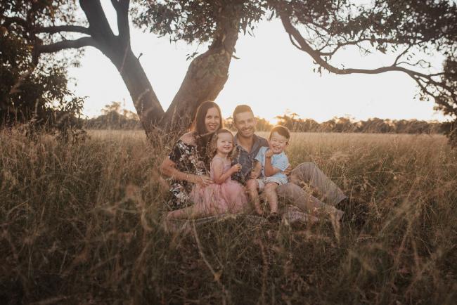 Family of four sitting under trees during Perth maternity photography session during golden hour at Perry's Paddock