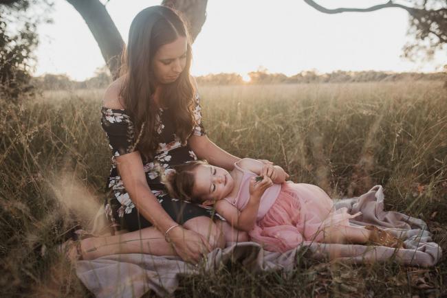 Daughter laying on pregnant mothers lap during Perth maternity photography session during golden hour at Perry's Paddock
