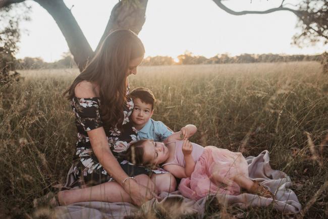 Pregnant mother sitting on blanket with son and daughter during Perth maternity photography session during golden hour at Perry's Paddock