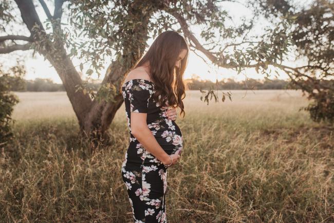 Pregnant woman standing by trees during Perth maternity photography session during golden hour at Perry's Paddock