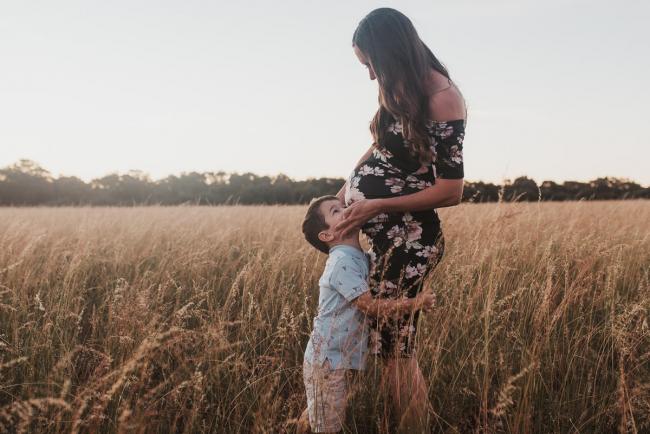 Boy hugging his pregnant mothers legs during Perth maternity photography session during golden hour at Perry's Paddock