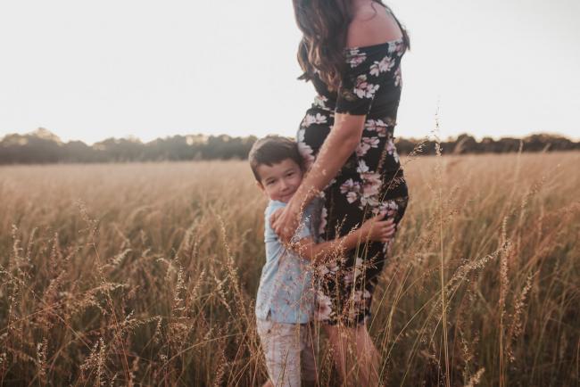 Boy hugging his pregnant mothers legs during Perth maternity photography session during golden hour at Perry's Paddock