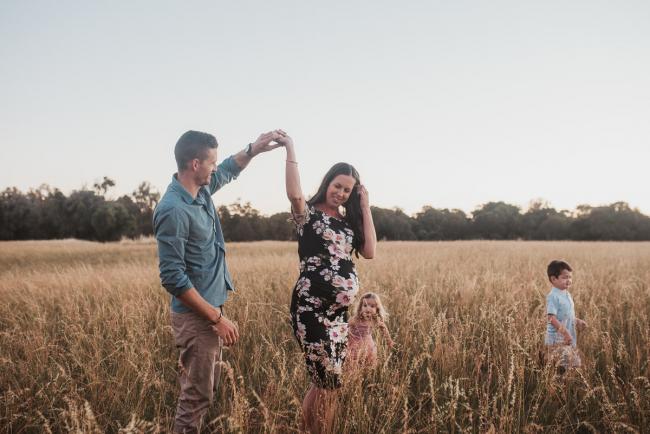 Mother and father dancing as son and daughter play behind them during Perth maternity photography session during golden hour at Perry's Paddock