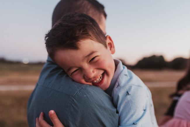 Boy smiling over dad's shoulder during Perth maternity photography session during golden hour at Perry's Paddock