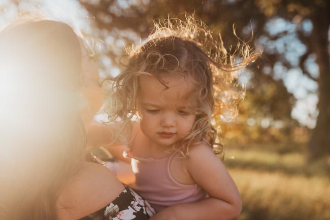 Little girl with curls blowing in the wind during Perth maternity photography session during golden hour at Perry's Paddock