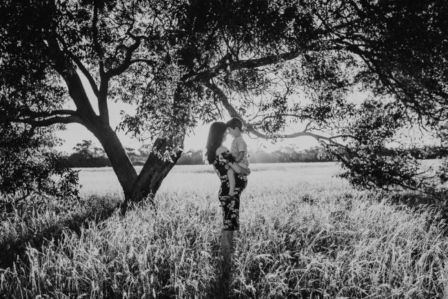 black and white image of pregnant mother holding son under trees during Perth maternity photography session during golden hour at Perry's Paddock