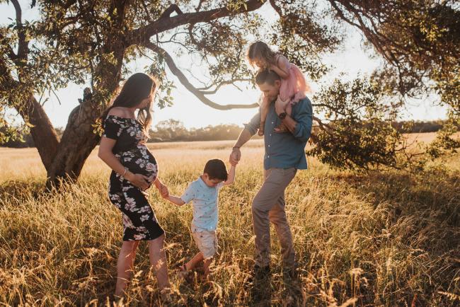Father with daughter on his shoulders whilst both parents hold hands with their son during Perth maternity photography session during golden hour at Perry's Paddock