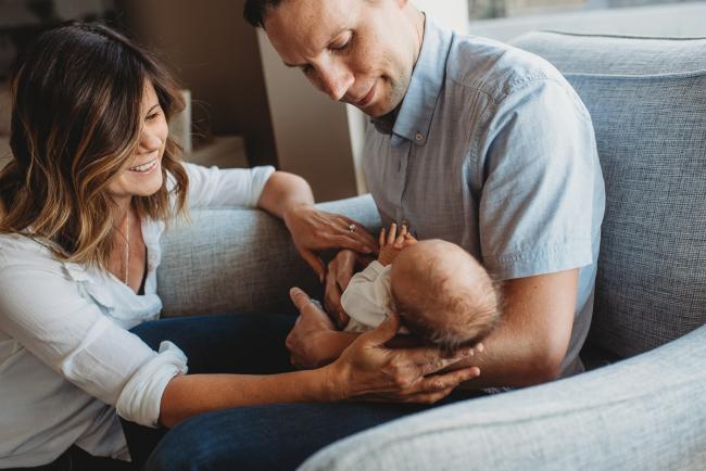 father holding newborn baby on chair while mother sits next to them with Perth newborn lifestyle photographer