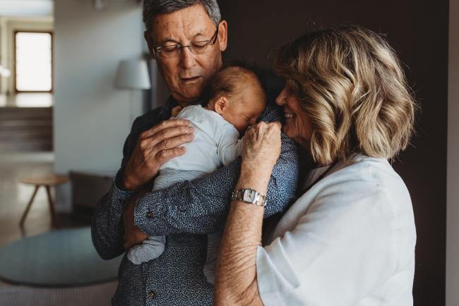 Newborn-Lifestyle-Photographer-Perth-17-of-50 Grandfather holding newborn baby as grandmother reaches in to kiss him during Perth lifestyle newborn photography session