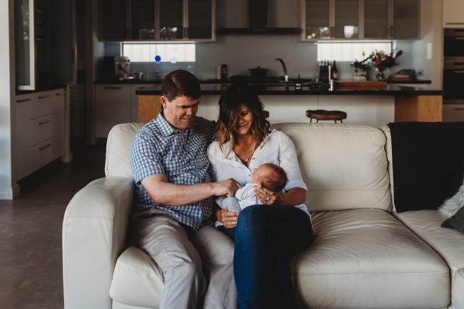 Newborn-Lifestyle-Photographer-Perth-21-of-50 Mother holding newborn baby on couch next to baby's uncle during Perth lifestyle newborn photography session