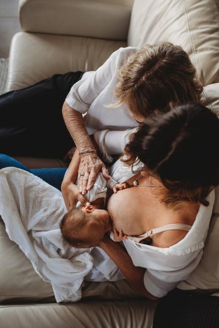 Newborn-Lifestyle-Photographer-Perth-23-of-50 top down image of mother breastfeeding on couch with grandmother next to them during Perth lifestyle newborn photography session