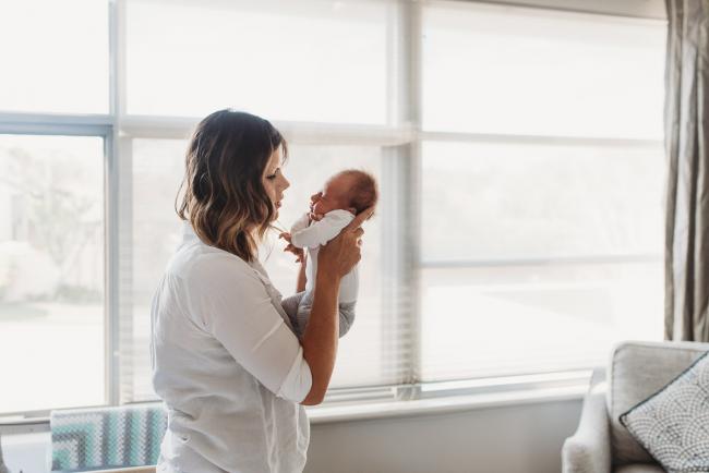 mother holding up newborn baby by window with Perth newborn lifestyle photographer