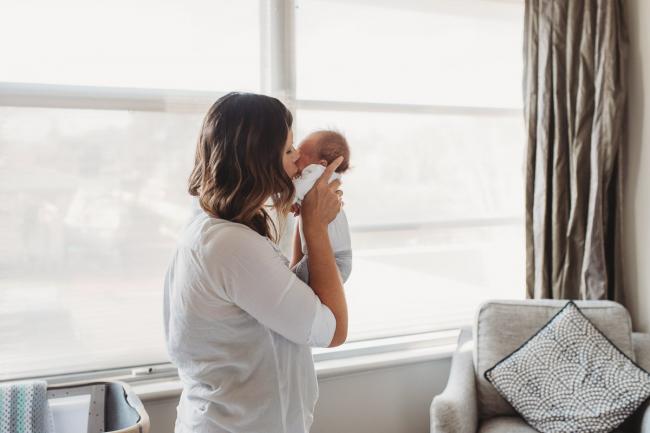 Newborn-Lifestyle-Photographer-Perth-29-of-50 mother holding and kissing newborn baby by window during Perth lifestyle newborn photography session