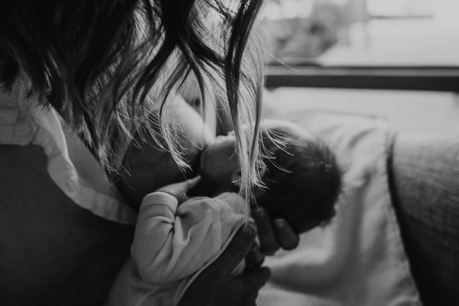 black and white image of mother breastfeeding newborn baby with her hair falling in the light during Perth lifestyle newborn photography session