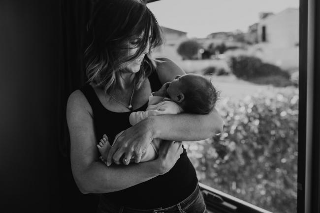 Black and white image of mother holding baby by a window with Perth newborn lifestyle photographer