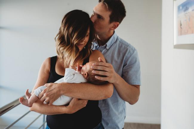 Newborn-Lifestyle-Photographer-Perth-45-of-50 Father kissing mother as she holds newborn baby during Perth lifestyle newborn photography session