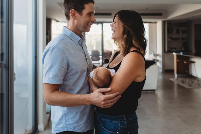 Newborn-Lifestyle-Photographer-Perth-49-of-50 Parents laughing at each other as they hold newborn baby during Perth lifestyle newborn photography session