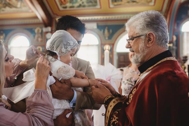 Perth-Events-Photographer-Christening-16-of-25 Mother doing up necklace on little girl and Priest touching her hands at baptism at Macedonian Orthodox Church with Perth events photographer