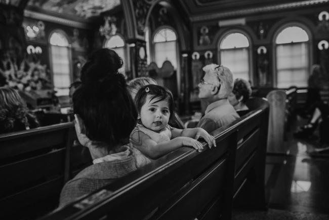 black and white image of little girl looking over a pew at baptism at Macedonian Orthodox Church with Perth events photographer