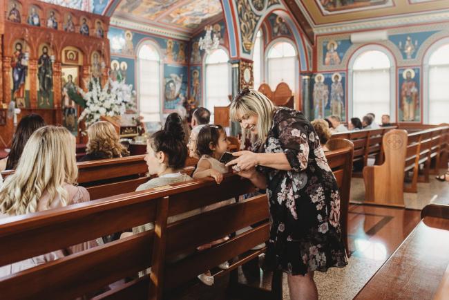 Perth-Events-Photographer-Christening-5-of-25 Woman showing little girl her phone at the pews at baptism at Macedonian Orthodox Church with Perth events photographer