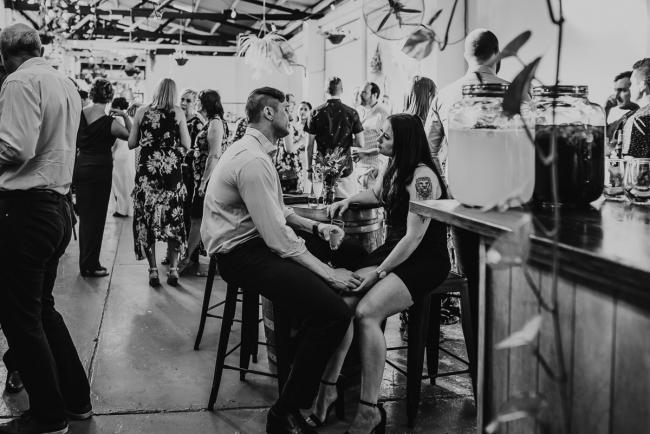 black and white image of couple sitting at bar table and holding hands during a party at Cleaver St Event Space with Perth events photographer
