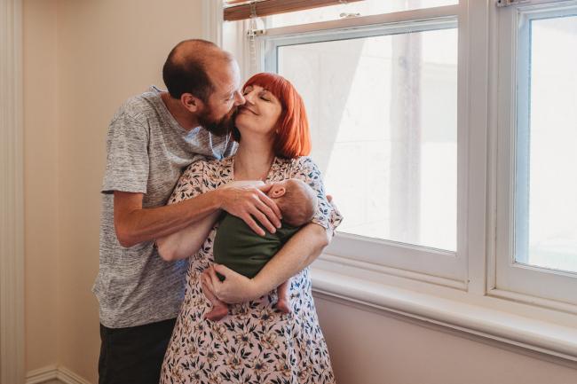 Parents kissing as they hold their newborn baby during newborn photography Perth session