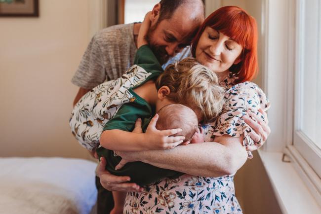 Parents holding toddler who is kissing newborn baby brother during newborn photography Perth session