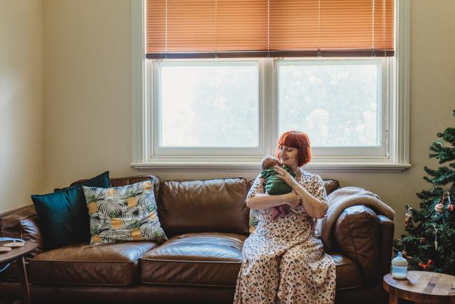 Mother burping newborn baby on couch during in-home Perth newborn lifestyle photography session