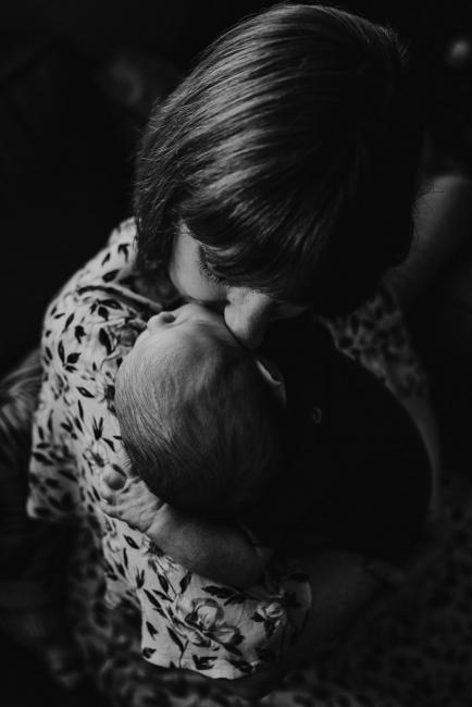 black and white image of mother kissing newborn baby who is on her shoulder during in-home Perth newborn lifestyle photography session
